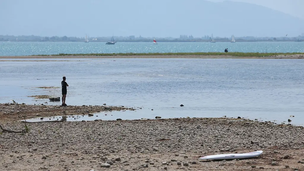 Es-bleibt-heiss-in-Bayern-Ein-Mann-steht-am-trockenen-Ufer-des-Bodensees-neben-einem-Surfboard