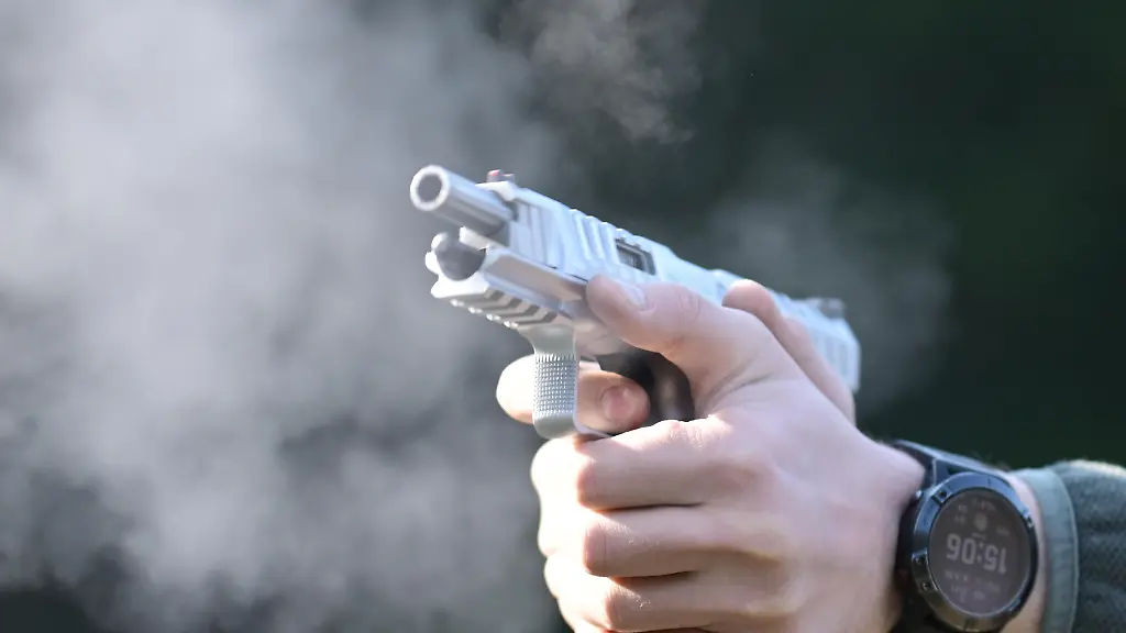 Male-shooter-wearing-a-camouflage-cap-and-sunglasses-fires-a-semi-automatic-pistol-at-an-outdoor-shooting-range-producing-muzzle-smoke-Image-conveys-training-marksmanship-tactical-practice-and-firearm-safety