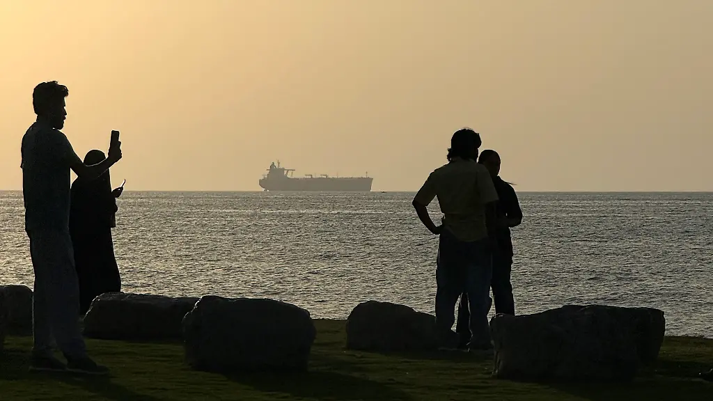 People-enjoy-the-beach-as-a-vessel-is-seen-waiting-to-cross-the-Strait-of-Hormuz-in-the-Arabian-Sea-off-Muscat-Oman-Tuesday-May-12-2026-The-fragile-cease-fire-between-the-United-States-and-Iran-conditioned-on-opening-the-strait-has-sharply-reduced-maritime-traffic-with-tensions-mounting-in-negotiations-between-the-two-sides