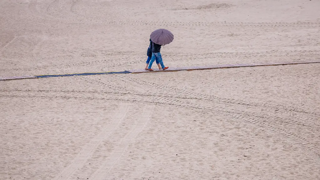 Unter-einem-Regenschirm-sind-Urlauber-am-Strand-von-Warnemuende-unterwegs-Mit-niedrigen-Temperaturen-und-teilweise-kraeftigen-Regenschauern-zeigt-sich-das-Sommerwetter-in-Norddeutschland-von-seiner-unfreundlichen-Seite