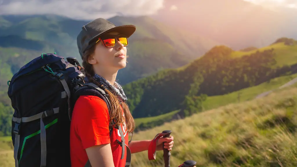 Ein-Tourist-Maedchen-mit-einem-Rucksack-bewundert-den-Sonnenuntergang-vom-Berghang-Reisende-im-Hintergrund-der-Berge-und-Wolken-bei-Sonnenuntergang-Frau-Tourist-in-Sonnenbrille-Muetze-und-mit-einem-Rucksack-steht-auf-dem-Hang-des-Berges-Trekking-und-Wandern-auf-dem-Berg-A-tourist-girl-with-a-backpack-admires-the-sunset-from-the-mountainside-Traveler-in-the-background-of-mountains-and-clouds-at-sunset-Woman-tourist-in-sunglasses-cap-and-with-a-backpack-stands-on-the-slope-of-the-mountain-Trekking-and-hiking-in-the-mo-Copyright-imageBROKER-IanxIankovskii-ibxiqx09618105