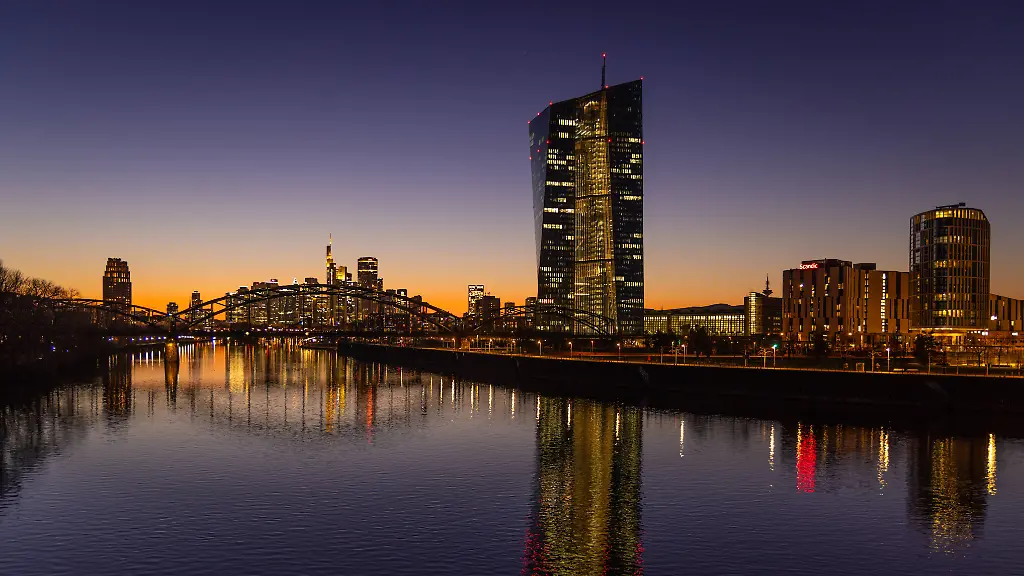 Die-Europaeische-Zentralbank-EZB-und-die-Frankfurter-Skyline-Die-Lichter-in-den-Bueros-der-Europaeischen-Zentralbank-EZB-und-der-Frankfurter-Skyline-leuchten-am-Abend-nach-Sonnenuntergang