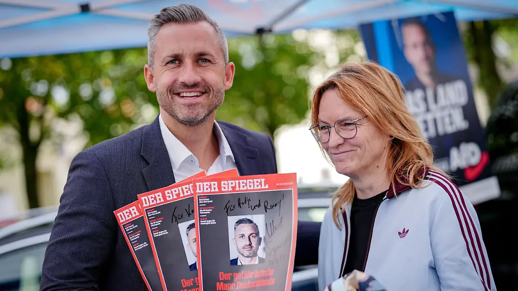 Wiederholung-mit-geaenderten-Verwendungsrechten-Ulrich-Siegmund-AfD-Spitzenkandidat-fuer-die-Landtagswahl-in-Sachsen-Anhalt-zeigt-auf-dem-Marktplatz-in-Oranienbaum-signierte-Spiegel-Magazine-Cover-neben-einer-Besucherin