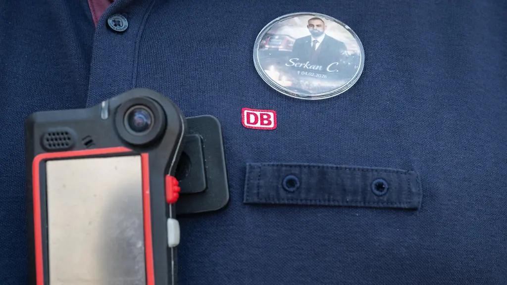 Ein-Zugbegleiter-traegt-einen-Anstecker-mit-dem-Bild-des-verstorbenen-Zugbegleiters-und-eine-Bodycam-Fuenf-Monate-nach-dem-brutalen-Angriff-auf-einen-Zugbegleiter-in-Rheinland-Pfalz-ist-der-Angeklagte-zu-zehn-Jahren-Gefaengnis-verurteilt-worden