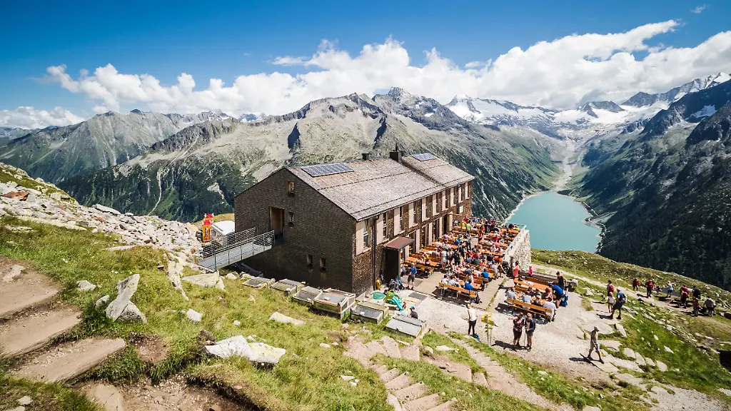 Tourists-have-rest-at-Olpererhutte-mountain-hut-in-Zillertal-in-Austrian-Alps-with-beautiful-scenery-view-above-lake