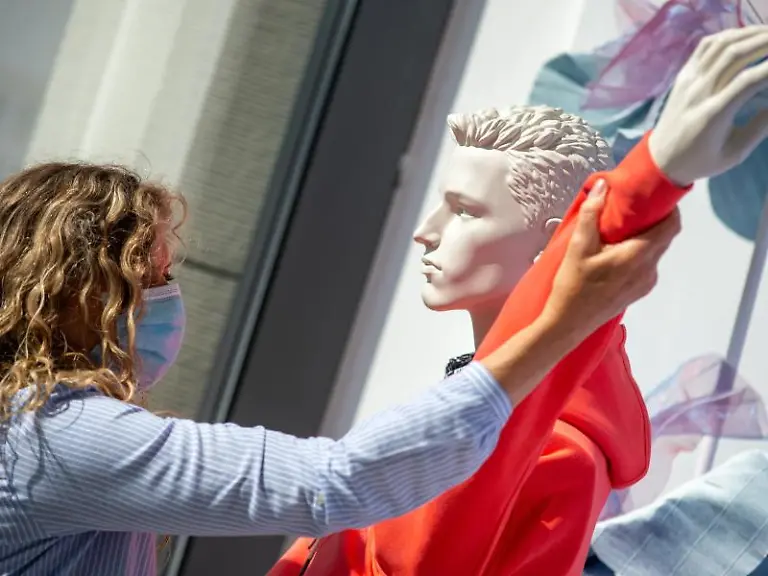 Eine-Verkaeuferin-mit-einem-Mund-Nasen-Schutz-entkleidet-eine-Puppe-in-einem-Schaufenster