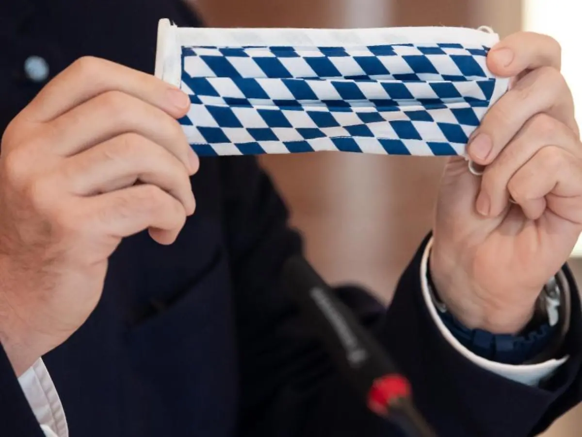 Ministerpraesident-Markus-Soeder-CSU-haelt-einen-Mundschutz-mit-der-bayerischen-Flagge-in-den-Haenden