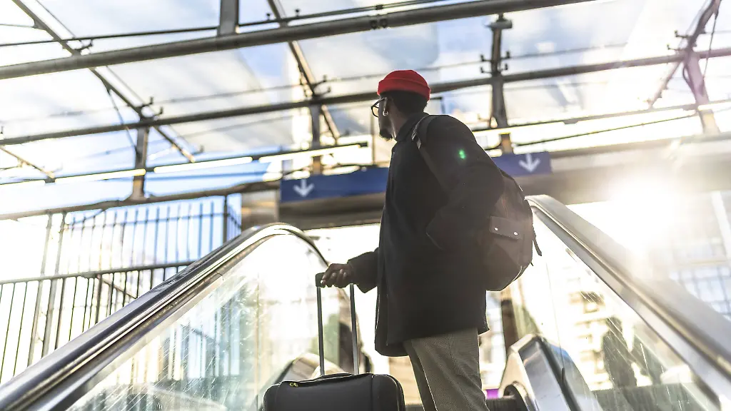 Mann mit Koffer auf Rolltreppe