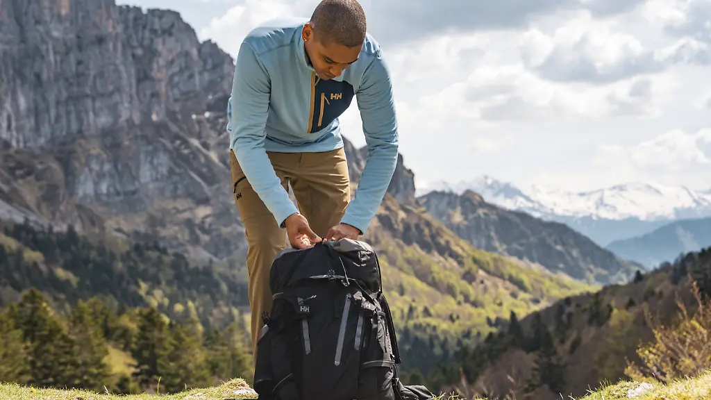 Mann packt Rucksack beim Wandern und trägt eine Jacke von Helly Hansen
