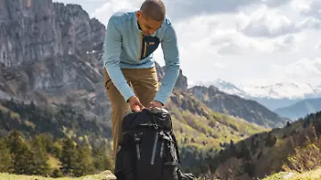 Mann packt Rucksack beim Wandern und trägt eine Jacke von Helly Hansen