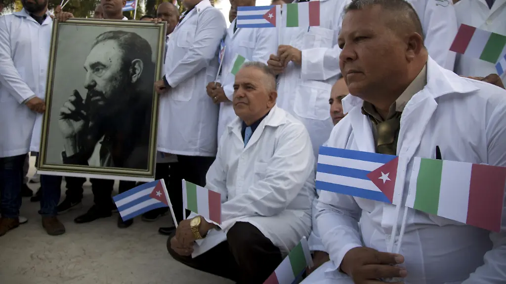 Kubanische-Hilfskraefte-lassen-sich-mit-einem-Foto-von-Fidel-Castro-sowie-kubanischen-und-italienischen-Landesflaggen-vor-ihrer-Reise-nach-Italien-fotografieren