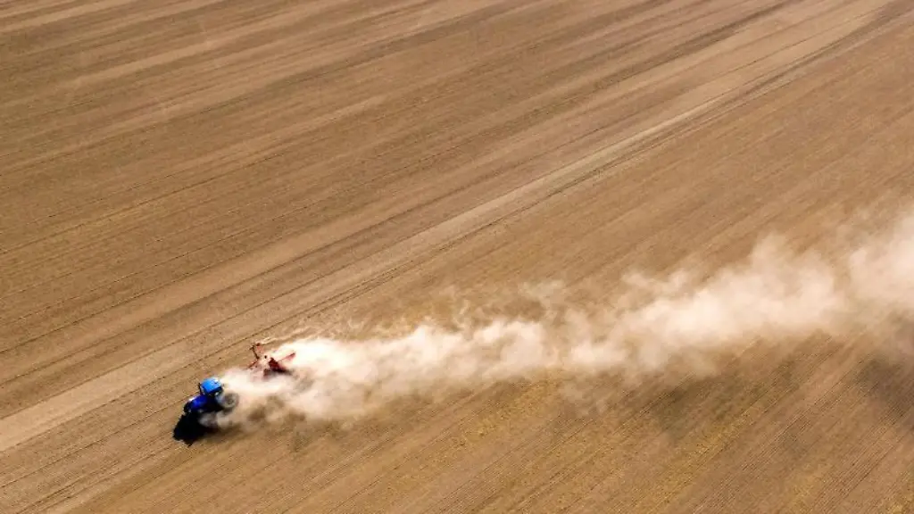 Ein-Traktor-faehrt-mit-einer-Saemaschine-ueber-ein-Feld-und-zieht-eine-Staubwolke-hinter-sich-her