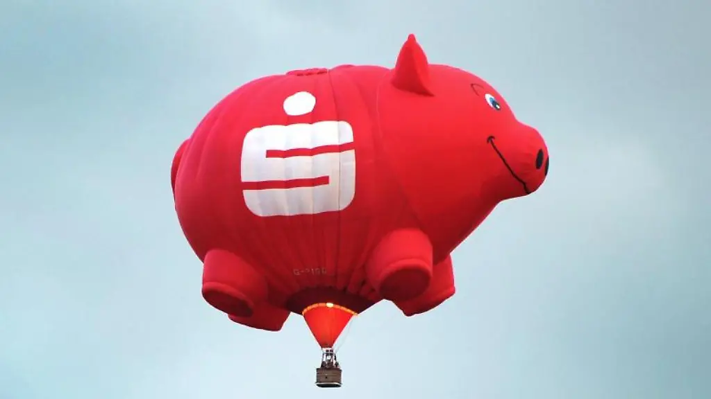 Ein-Heissluftballon-in-der-Form-eines-Sparschweines-mit-einem-Sparkassen-Logo-ist-am-Himmel-zu-sehen