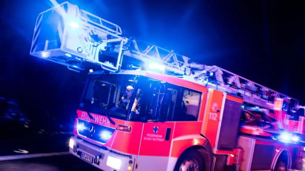 Ein-Drehleiterwagen-der-Feuerwehr-faehrt-mit-Blaulicht-ueber-eine-Strasse