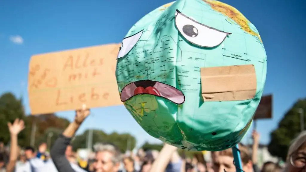 Demonstranten-halten-einen-Luftballon-mit-Globusaufdruck-hoch-der-mit-einem-Pflaster-und-ungluecklichen-Gesichtszuegen-beklebt-ist
