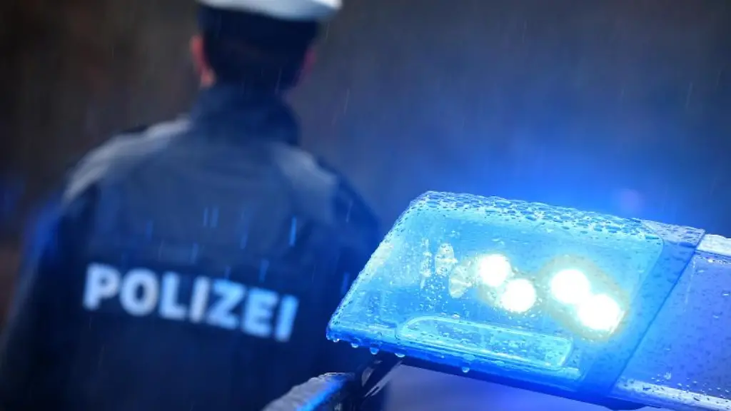 Ein-Polizist-steht-im-Regen-vor-einem-Streifenwagen-dessen-Blaulicht-aktiviert-ist