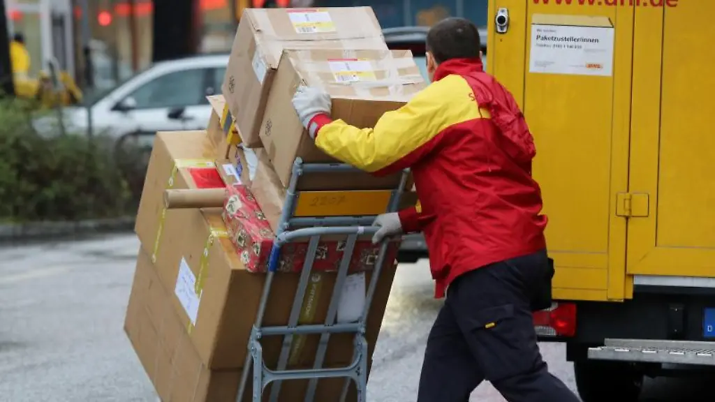 Ein-Paketbote-der-Post-schiebt-eine-Sackkarre-mit-Paketen-ueber-Strasse