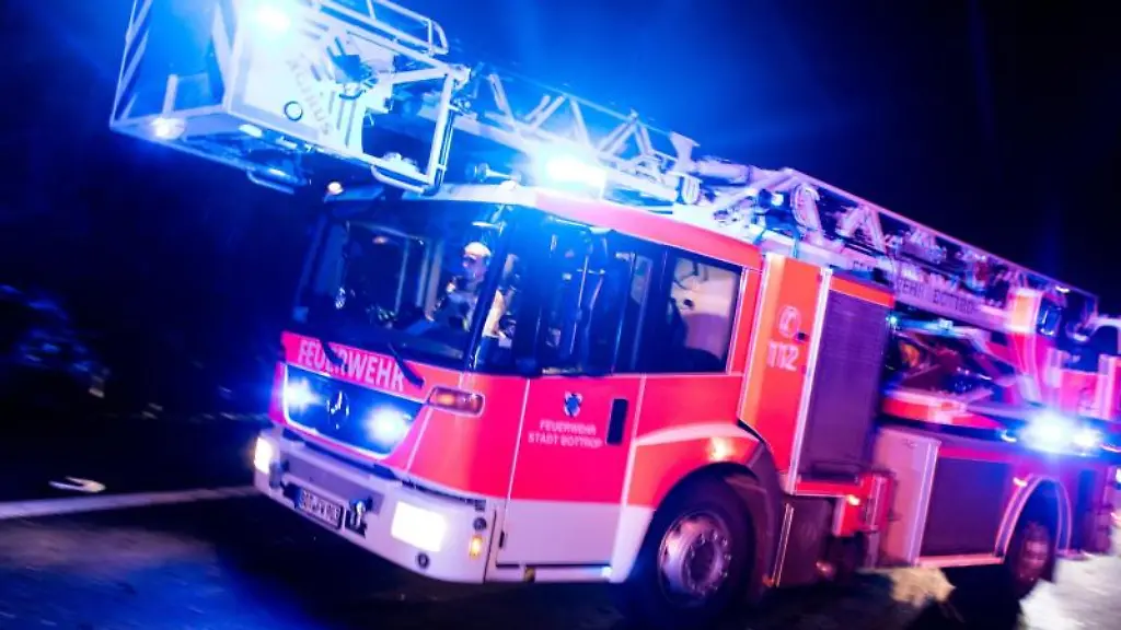 Ein-Drehleiterwagen-der-Feuerwehr-faehrt-mit-Blaulicht-an-einer-Unfallstelle-vorbei