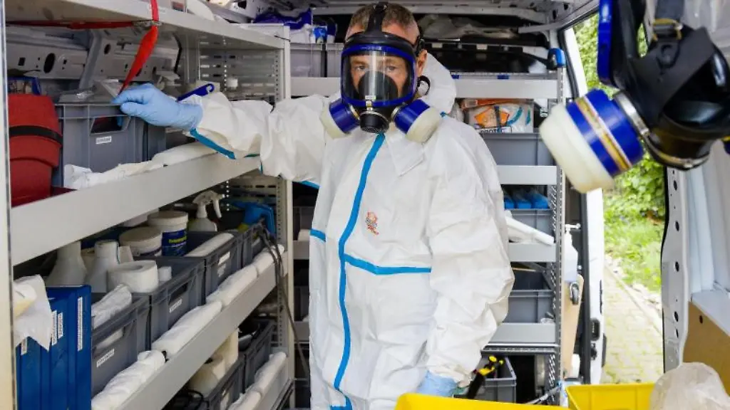 Tatortreiniger-Dirk-Plaehn-steht-in-Schutzanzug-und-mitAtemmaske-in-seinem-Einsatzfahrzeug