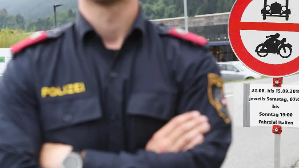 Ein-Polizist-steht-vor-einem-Schild-das-auf-die-Sperrung-fuer-den-Verkehr-mit-Fahrziel-Italien-hinweist