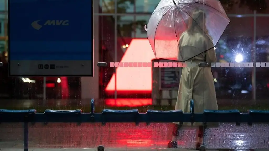 Eine-Frau-wartet-mit-ihrem-Regenschirm-an-einer-Bushaltestelle-auf-den-Bus