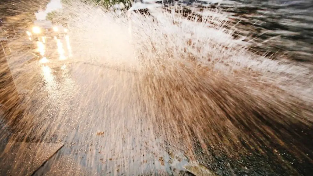 Ein-Auto-faehrt-in-der-Landeshauptstadt-durch-eine-Wasserlache-auf-der-Strasse