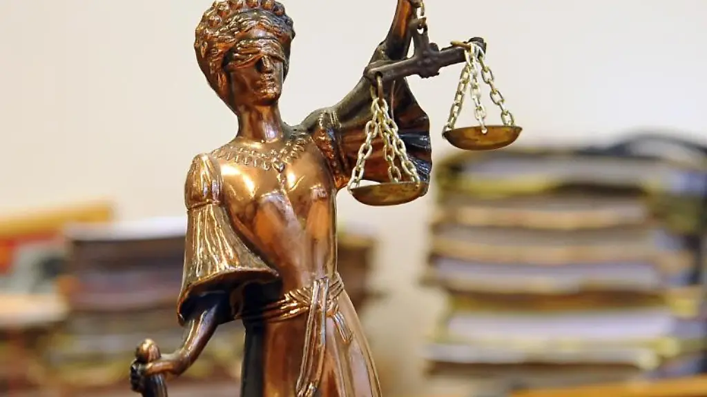 Eine-goldfarbene-Justitia-Figur-steht-vor-Aktenbergen