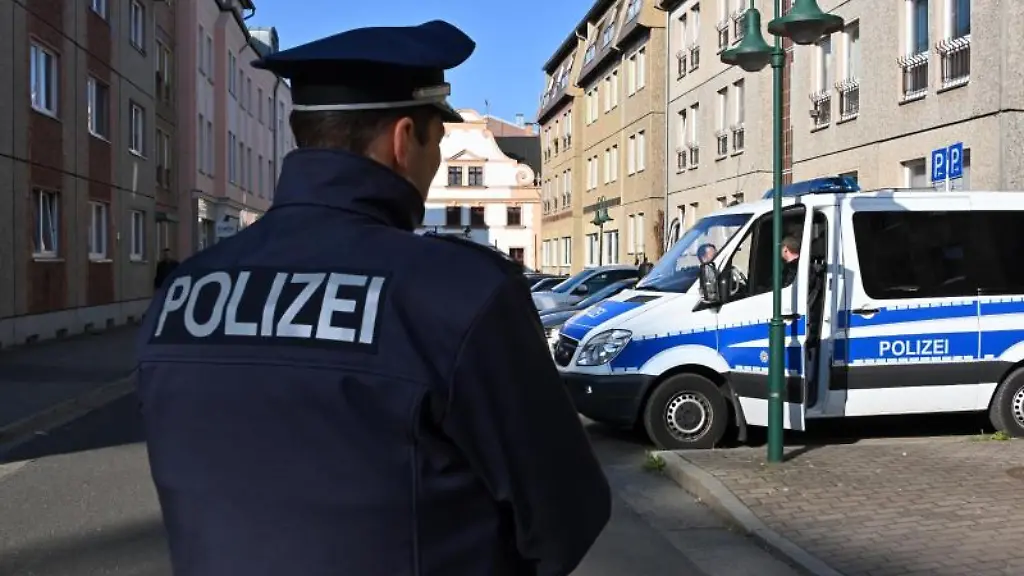 Ein-Polizist-steht-auf-der-Strasse-im-Hintergrund-steht-ein-Einsatzfahrzeug-der-Polizei