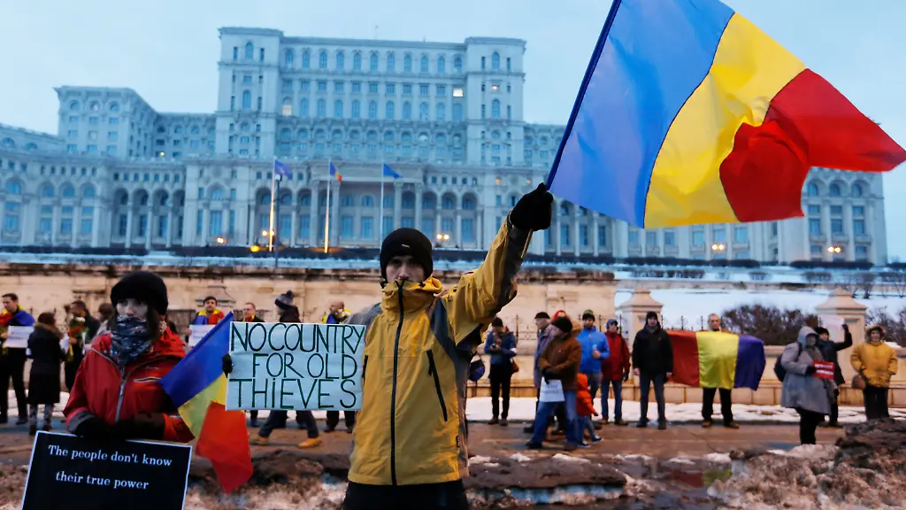 Demonstranten-stehen-am-04-02-2017-in-Bukarest-Rumaenien-vor-dem-Parlamentspalast-Ein-junger-Mann-schwenkt-dabei-eine-Flagge-in-den-Nationalfarben-und-haelt-ein-Schild-mit-der-Aufschrift-No-country-for-old-thieves-Kein-Land-fuer-alte-Diebe-In-Rumaenien-demonstrieren-Zehntausende-Menschen-landesweit-den-fuenften-Tag-in-Folge-gegen-die-sozialliberale-Regierung-Ausloeser-der-Proteste-ist-eine-Eilverordnung-die-die-Justiz-bei-der-Verfolgung-von-Korruption-einschraenkt