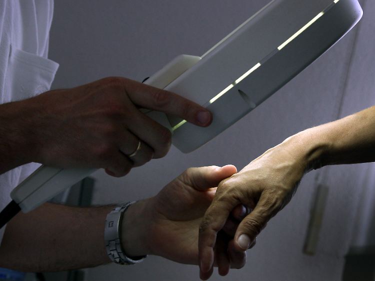 Ein Hautarzt untersucht mit einem Vergrößerungsglas die Haut einer Patientin bei einer Hautkrebs-Früherkennung.