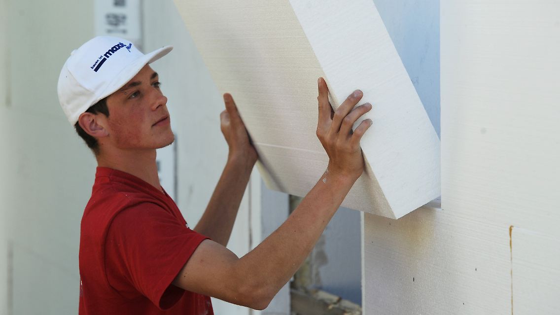 Ein Handwerker montiert eine Styroporplatte zur Wärmedämmung an eine Fassade.