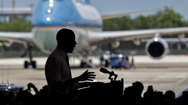 Obama spricht in einem Hangar. Im Hintergrund die Präsidentenmaschine Air Force One.
