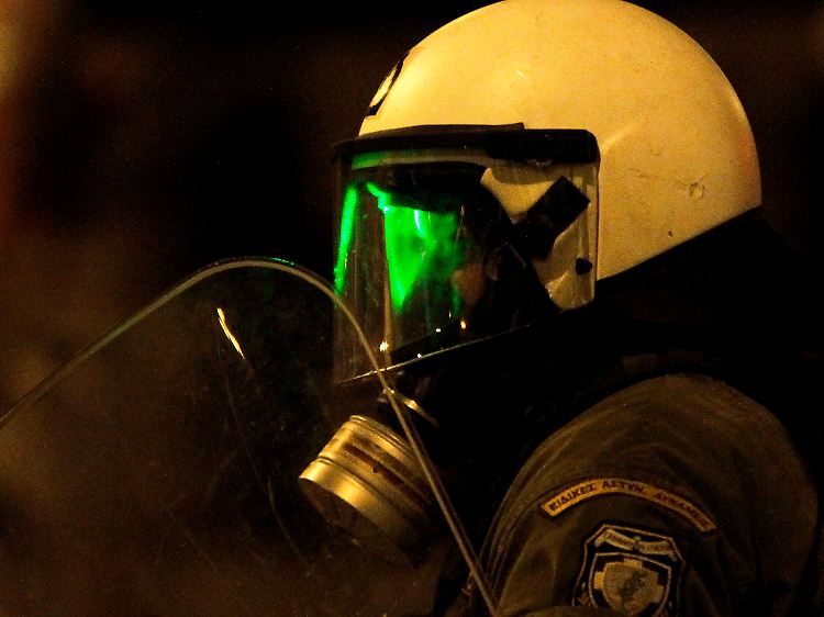 Ein Demonstrant zielt mit einem Laser auf einen griechischen Polizisten.