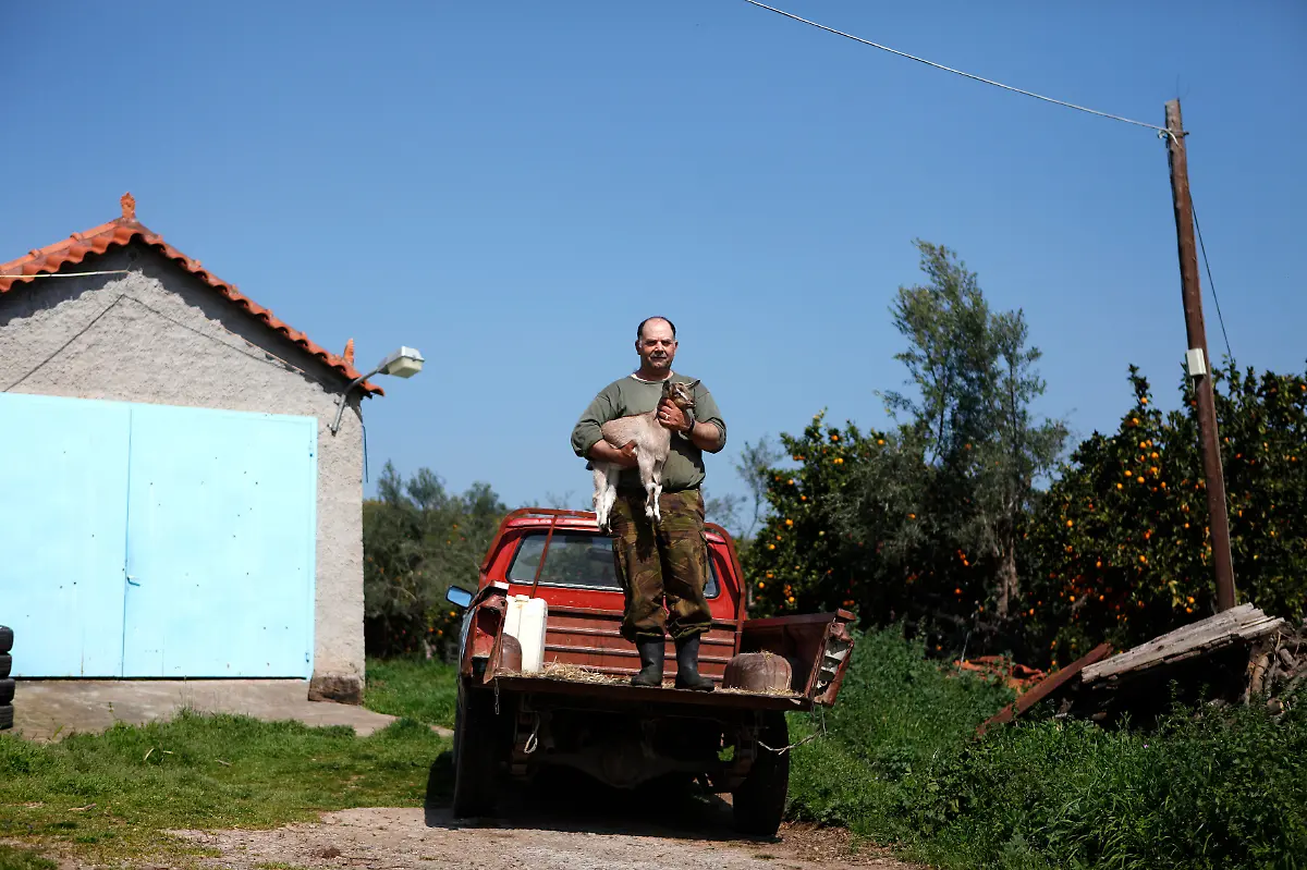 George-Andrianakis-56-a-farmer-stands-on-the-back-of-his-pickup-truck-with-one-of-his-kid-goats-in-the-yard-of-his-farm-at-the-village-of-Stafania-in-the-Peloponesse-area-of-Greece-March-17-2012-When-asked-how-he-had-been-affected-by-the-economic-crisis-Andrianakis-replied-I-am-surviving-rather-than-living-Picture-taken-March-17-2012
