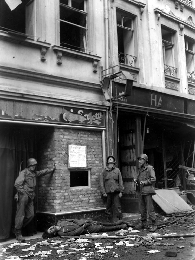 Drei US-Soldaten im April 1945 in Aschaffenburg. Neben ihnen liegt ein Wehrmachtssoldat, der in den letzten Kriegstagen aufgehängt worden war. Die GIs haben den Deutschen abgeschnitten.