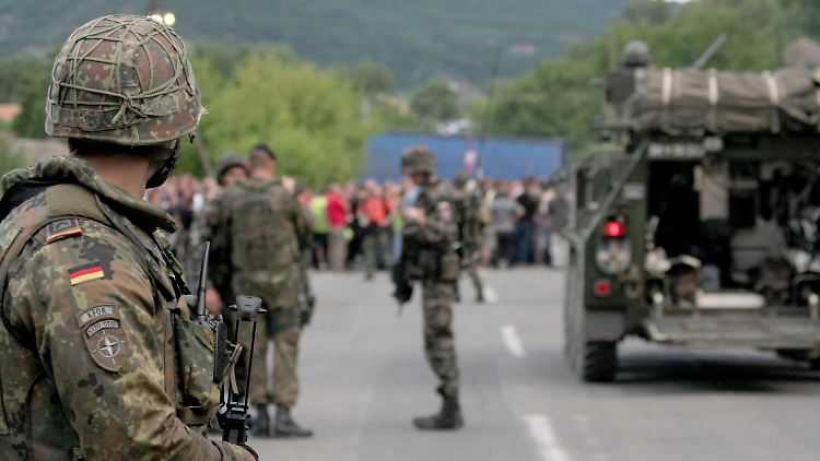 Ein Bundeswehrsoldat und slowenische KFOR-Soldaten vor einer Straßenblockade in Rudare.