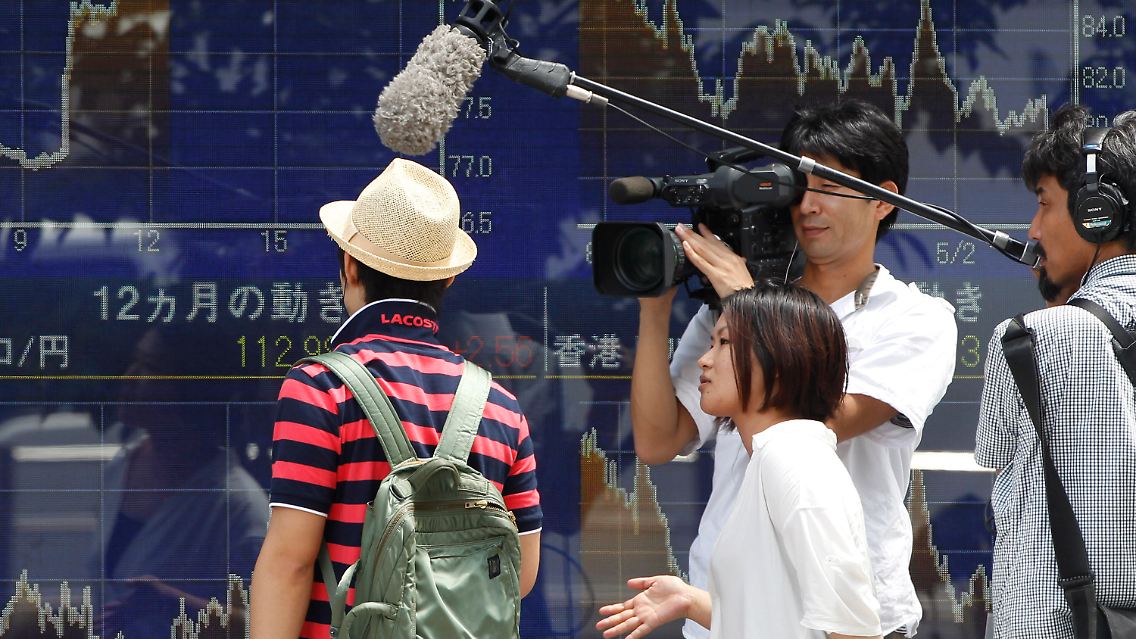 Vor der Börse in Tokio befragen Reporter einen Passanten.