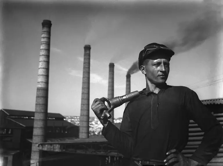 20465734-jpgHeroisch-wirkt-der-Produktionsarbeiter-in-der-fotografisch-gestellten-Pose-vor-rauchenden-Schornsteinen-mit-einem-Presslufthammer-ueber-der-Schulter-aufgenommen-1934-vor-der-Eisenhuette-in-Stalino-im-Donezbecken-Das-Foto-des-sowjetischen-Fotografen-Jewgeni-Chaldej-ist-in-dem-2008-erschienenen-Bildband-Der-bedeutende-Augenblick-veroeffentlicht