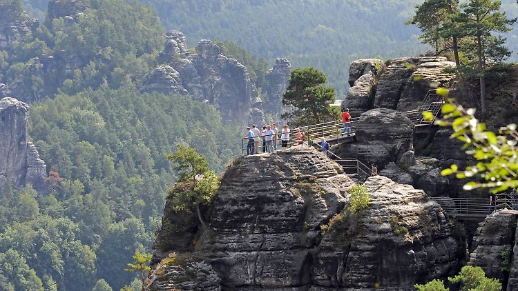 Jahr für Jahr stellt man sich die Frage: Wohin im Urlaub? (Wanderer in Rathen vor den Sandsteinfelsen der Sächsischen Schweiz)