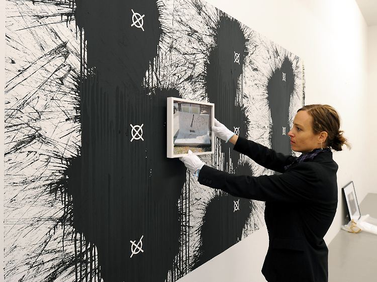Die Künstlerin Christine Würmell hält das Bild "Bilderahmen Landwehr" vor ihre Arbeit aus Acrylfarbe "Oberflächenaktiv II", die durch das Werfen von Farbeinheiten entstanden ist.