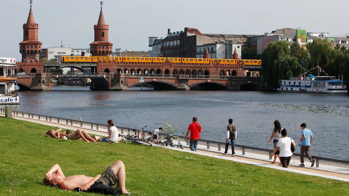 Ein paar kommen doch noch: Ein Tourist aus Finland genießt in Berlin auf einer Wiese hinter der East Side Gallery die Sonne. Im Hintergrund die Oberbaumbrücke.