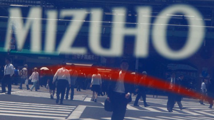 Im Firmenschild einer Niederlassung der Mizuho Financial Group in Tokio spiegeln sich die Passanten: Im Bericht zum ersten Quartal spiegeln sich dagegen die Schwierigkeiten, mit denen das Haus nach wie vor zu kämpfen hat.
