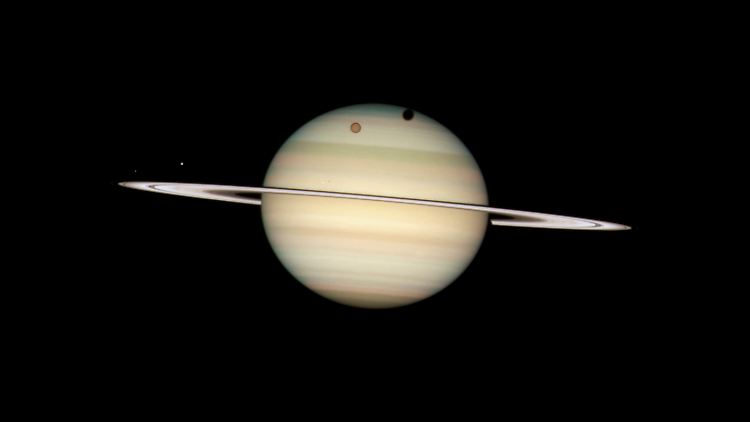 Der Titan (als Schatten oben zu sehen) kreist als größter Mond um den Saturn.