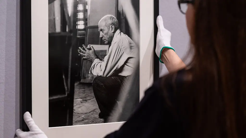 Eine-Mitarbeiterin-haengt-ein-eingerahmtes-Foto-von-Pablo-Picasso-des-Fotografen-Herbert-List-an-die-Wand