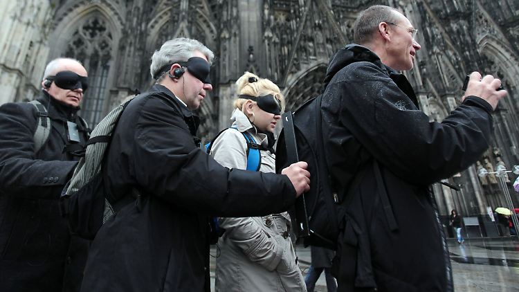 Teilnehmer eines "Blindwalk" gehen in Köln am Dom vorbei, geführt von Axel Rudolph.