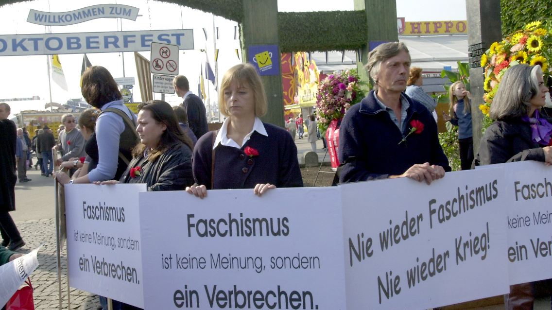 Demonstranten stehen am 20. Jahrestag des Anschlages vor dem Mahnmal am Haupteingang des Oktoberfestes.