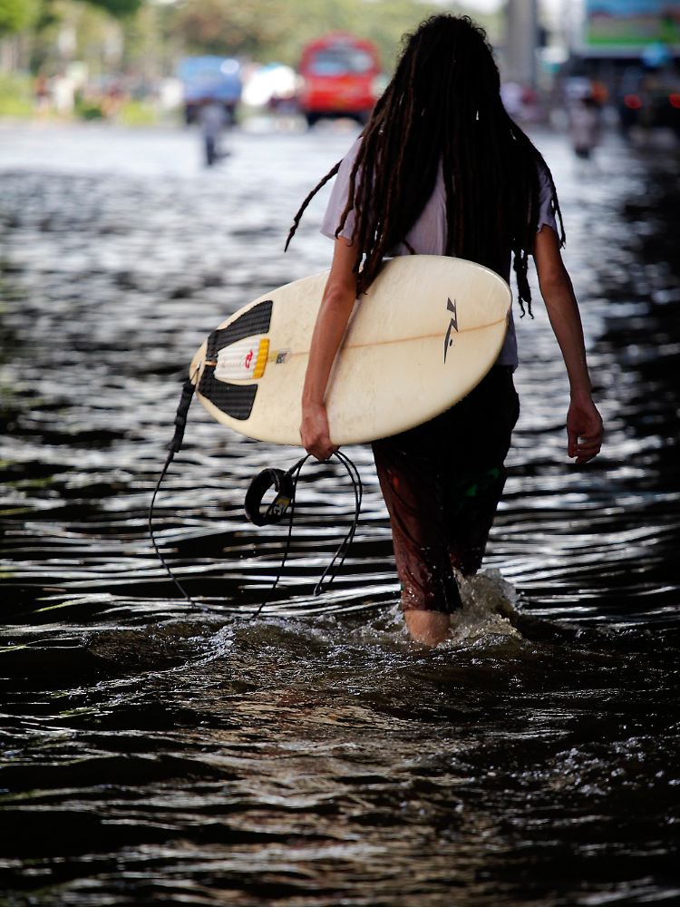 Ein Mann läuft mit seinem Surfboard durch die Straßen von Bangkok.
