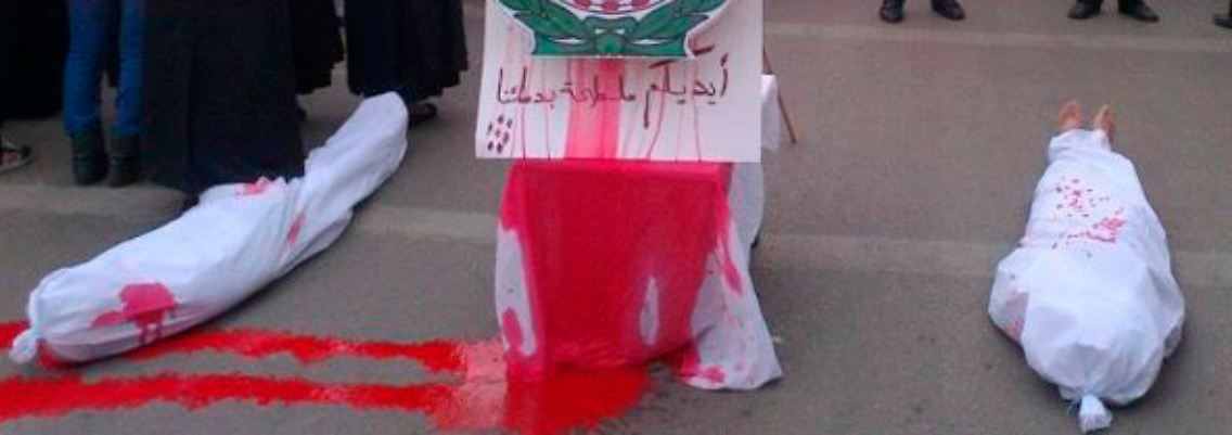 Proteste in Homs: Zwei Leichensäcke liegen neben einem Logo der Arabischen Liga.