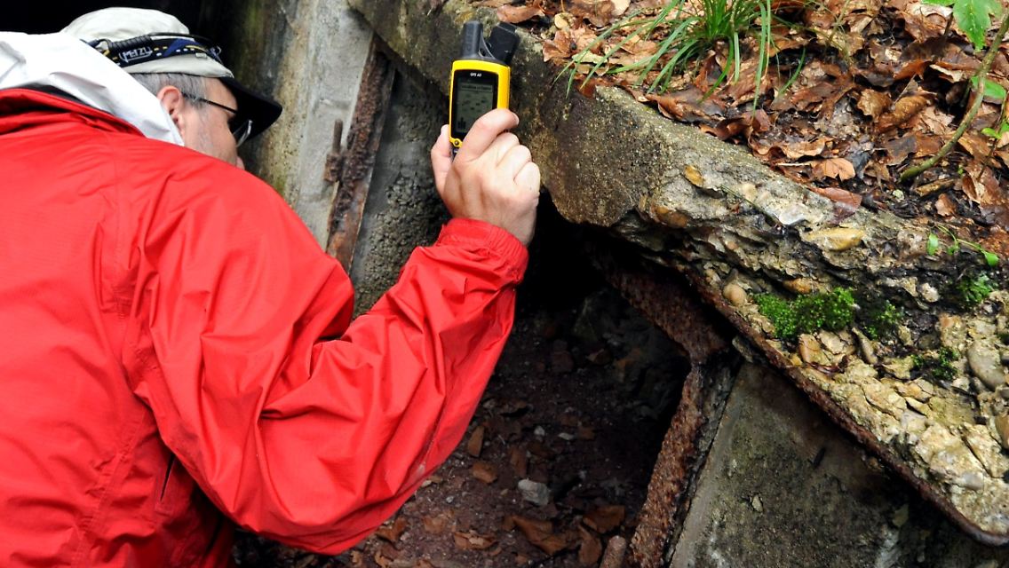 Ein "Geocacher" sucht vor dem Eingang eines Bunkers in einem Wald mit Hilfe eines Satellitennavigationsgerätes (GPS) ein verstecktes Behältnis, einen Cache ...