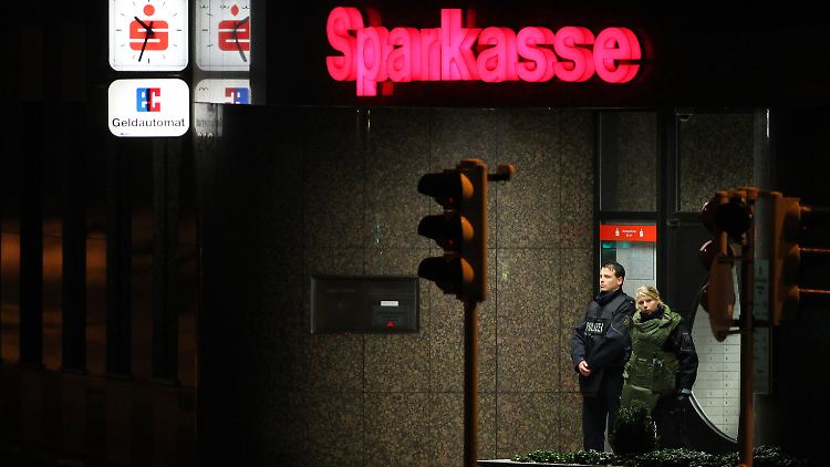 Beamte stehen in Schutzwesten vor der überfallenen Bank.
